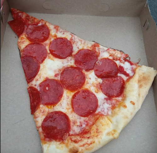 A slice of pepperoni pizza with melted cheese, resting in a cardboard box.