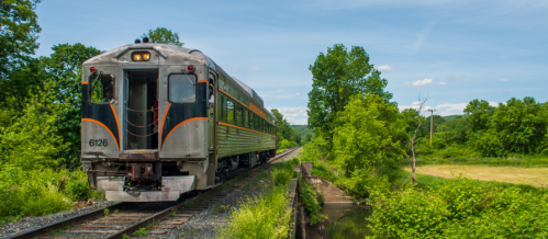 A vintage train on a scenic track surrounded by lush greenery and blue skies.