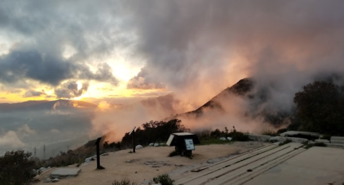 A scenic view of a mountain landscape at sunset, with clouds and mist enveloping the area.
