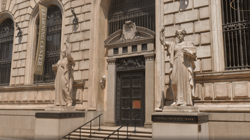 Exterior view of the Federal Reserve Bank, featuring two statues flanking the entrance and a banner for the library center.