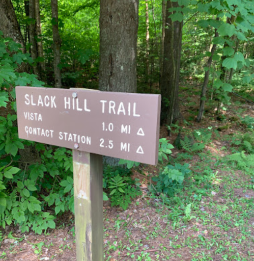 Sign for Slack Hill Trail indicating distances to Vista (1.0 miles) and Contact Station (2.5 miles) in a wooded area.