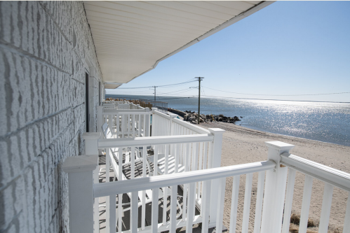 A view from a balcony overlooking a sandy beach and calm water under a clear blue sky.