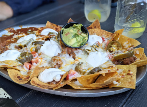 A platter of nachos topped with cheese, sour cream, guacamole, jalapeños, and diced tomatoes.