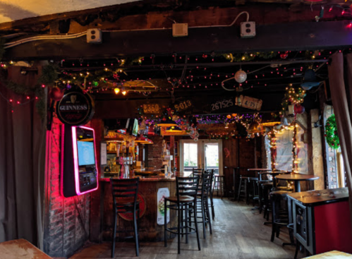 Cozy pub interior decorated with festive lights, featuring a bar, stools, and a warm, inviting atmosphere.