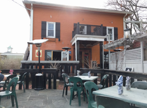 A two-story orange building with black shutters, surrounded by outdoor seating and patio heaters.