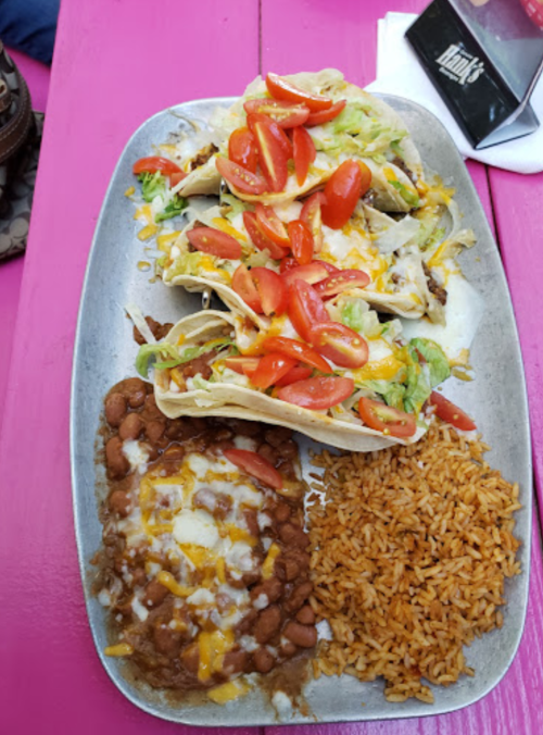 A platter featuring tacos topped with lettuce, tomatoes, and cheese, alongside rice and refried beans.