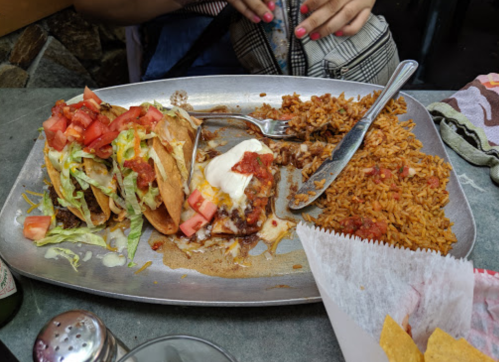 A silver platter with tacos topped with lettuce, tomatoes, and sour cream, alongside a serving of rice.