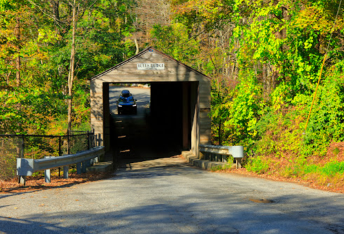 A wooden covered bridge surrounded by lush greenery, with a car approaching from the entrance.