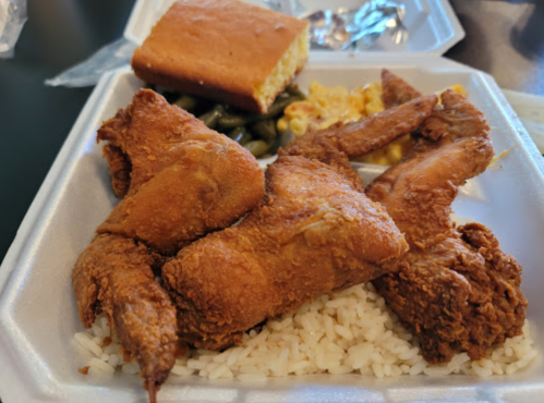 A takeout container with fried chicken wings, rice, macaroni and cheese, green beans, and cornbread.