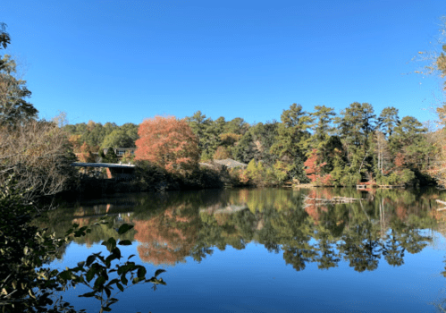 A serene lake surrounded by colorful autumn trees under a clear blue sky, reflecting the landscape in the water.
