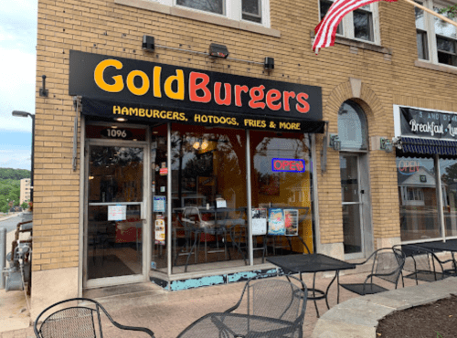 Exterior of GoldBurgers restaurant featuring a sign, outdoor seating, and an "Open" banner.