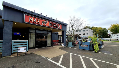 Exterior of Max Burger restaurant with a sign, outdoor seating, and a cloudy sky in the background.