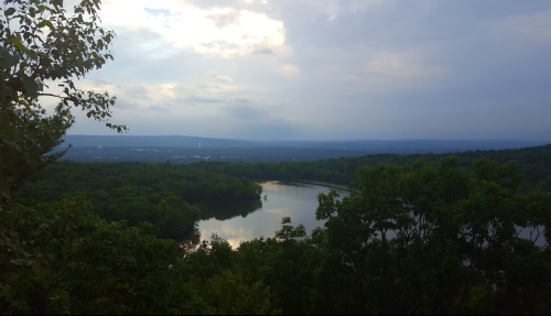 A serene landscape featuring a river winding through lush greenery under a cloudy sky.