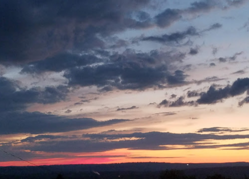 A colorful sunset with vibrant pink and orange hues against a backdrop of clouds and a fading blue sky.