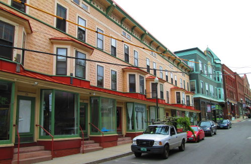 A street view of colorful buildings with shops and parked cars in a small town.