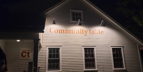 A well-lit building at night with the words "Community table" prominently displayed on the exterior wall.