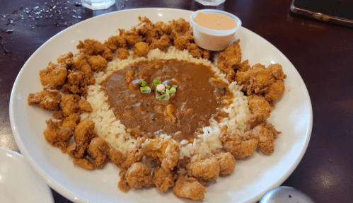 A plate of rice surrounded by crispy fried shrimp, with a serving of brown sauce and green onions in the center.