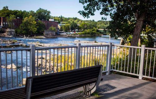A scenic view of a river with rocky banks, framed by trees and a bench in the foreground.