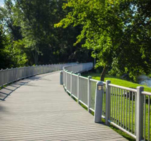 A winding pathway lined with a white fence, surrounded by lush greenery and trees.