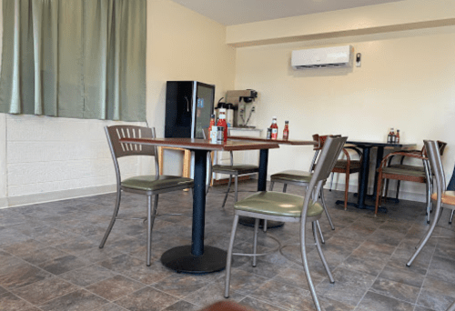 A small, empty dining area with a table and chairs, featuring a fridge and condiments on the table.