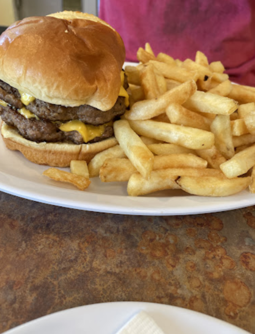 A close-up of a cheeseburger with two patties on a plate, accompanied by a side of golden French fries.