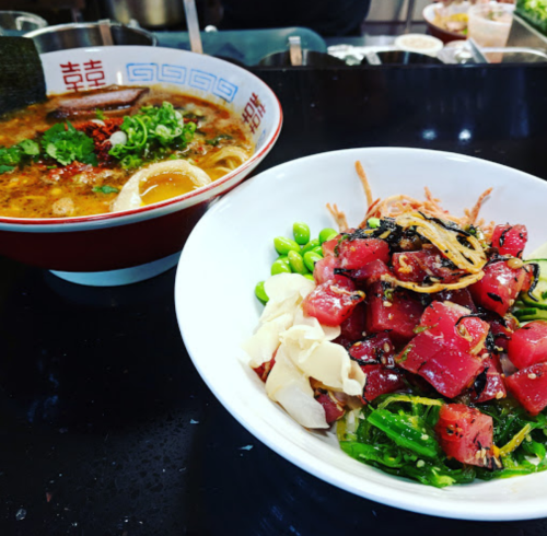 A bowl of ramen with broth and toppings next to a salad of tuna, seaweed, and vegetables on a black countertop.