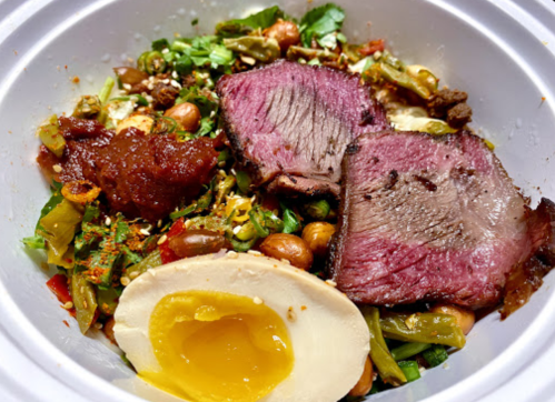 A bowl of salad topped with slices of beef, a soft-boiled egg, and various vegetables and garnishes.