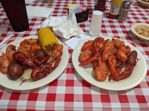 Two plates of crawfish and potatoes, with corn on the cob, on a red and white checkered tablecloth.