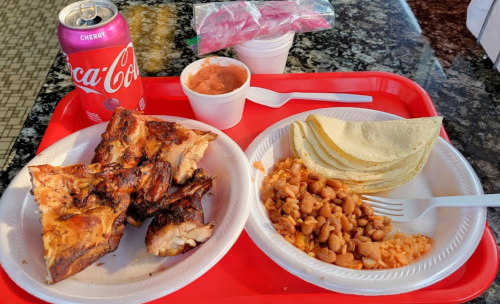 A tray with grilled chicken, rice, beans, tortillas, salsa, and a can of cherry Coca-Cola.