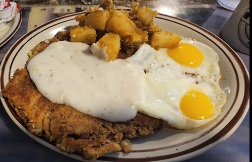 A plate of fried chicken with gravy, two sunny-side-up eggs, and seasoned hash browns.