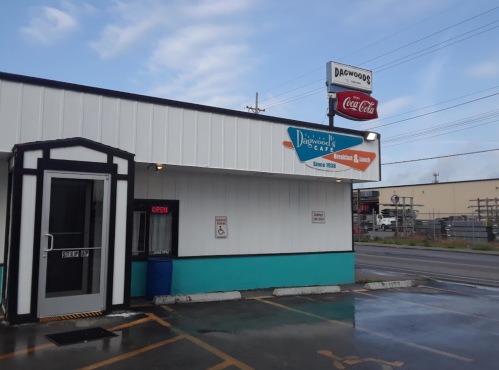 Exterior of Dagwood's Cafe with a sign, open door, and nearby Coca-Cola advertisement. Cloudy sky in the background.