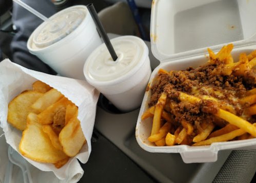 A takeout meal featuring fries topped with meat, a side of chips, and two drinks in cups.