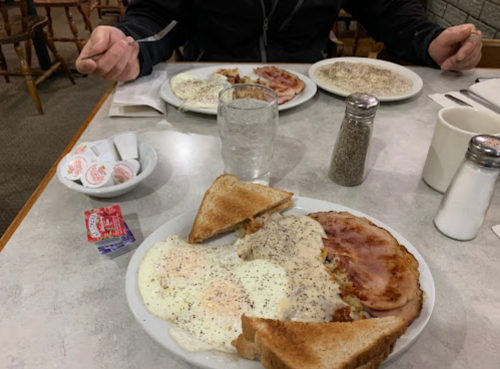 A table set with two plates of breakfast, featuring eggs, ham, hash browns, toast, and condiments.