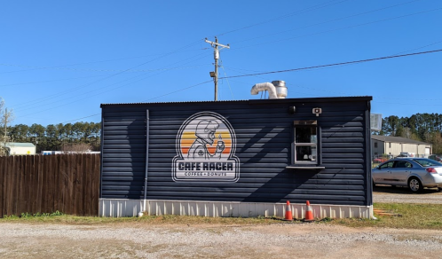 A small black building with a logo for "Café Racer Coffee & Donuts" and a drive-thru window.