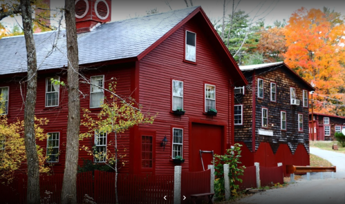 A scenic view of red wooden buildings surrounded by trees with autumn foliage.