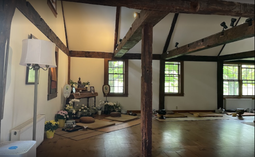 A serene room with wooden beams, natural light, and a meditation space adorned with flowers and cushions.