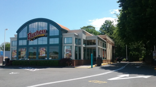 A fast-food restaurant named "Duchess" with large windows and outdoor seating, set in a parking lot on a sunny day.