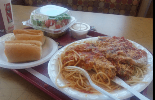 A tray with a plate of spaghetti and chicken, rolls, a salad, and a small cup of dressing.