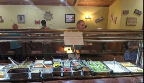 A buffet with various food options; a sign states children under 10 must be accompanied by an adult.
