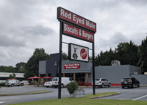 Sign for "Red Eyed Mule Biscuits & Burgers" outside a restaurant with cars parked and outdoor seating.