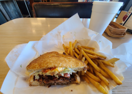 A sandwich with lettuce and tomato beside a pile of golden fries, with a large drink in the background.