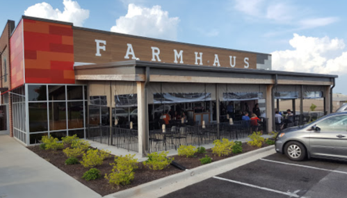 Exterior of a restaurant named "Farmhaus," featuring large windows, outdoor seating, and a modern design.