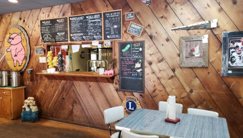 Interior of a rustic eatery with a wooden wall, menu board, and a table set for dining. Decor includes a pig illustration.