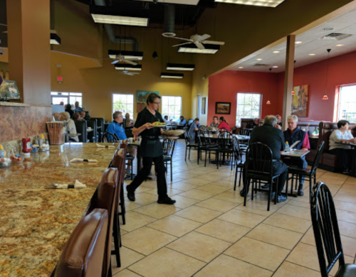 A busy restaurant interior with diners at tables and a server carrying food through the dining area.