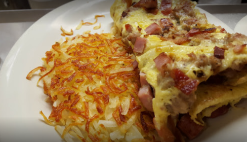 A plate featuring a hearty omelette filled with ham and sausage, alongside crispy golden hash browns.