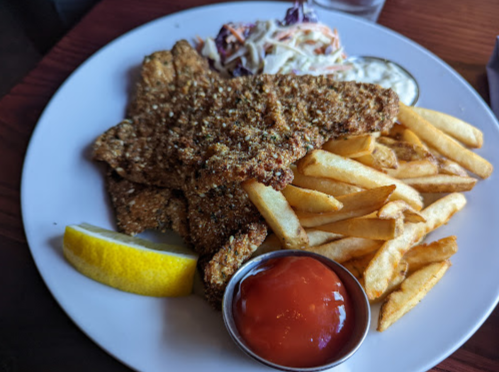 A plate of fried fish with coleslaw, French fries, a lemon wedge, and a small cup of ketchup.