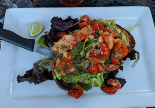 A plate of toasted bread topped with avocado, cherry tomatoes, and greens, garnished with lime wedges.