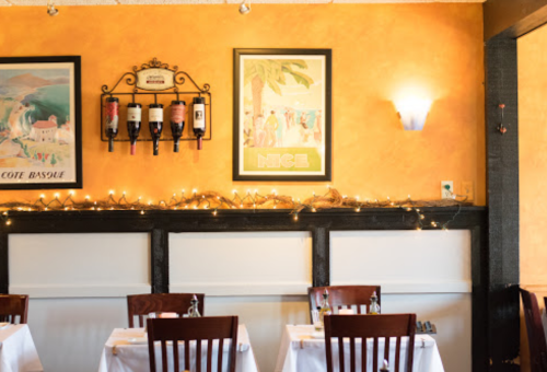 Cozy restaurant interior with orange walls, wine display, and twinkling lights above white tablecloths.