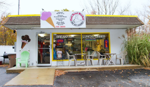 A small takeout restaurant with a colorful sign, featuring outdoor seating and a variety of menu items displayed in the window.