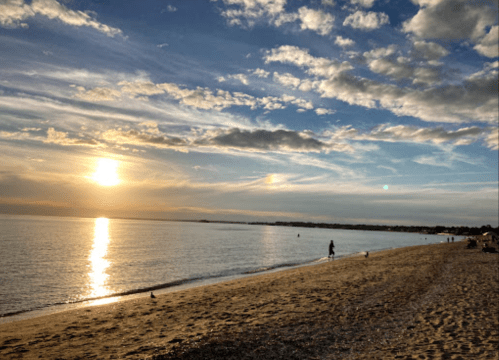 A serene beach at sunset, with gentle waves, a sandy shore, and a few people walking along the water's edge.